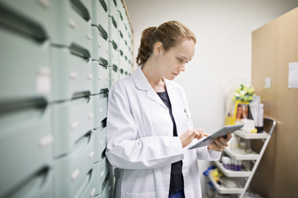 Dekorativ bild. Kvinnlig farmaceut i labbrock använder digital surfplatta i förråd.